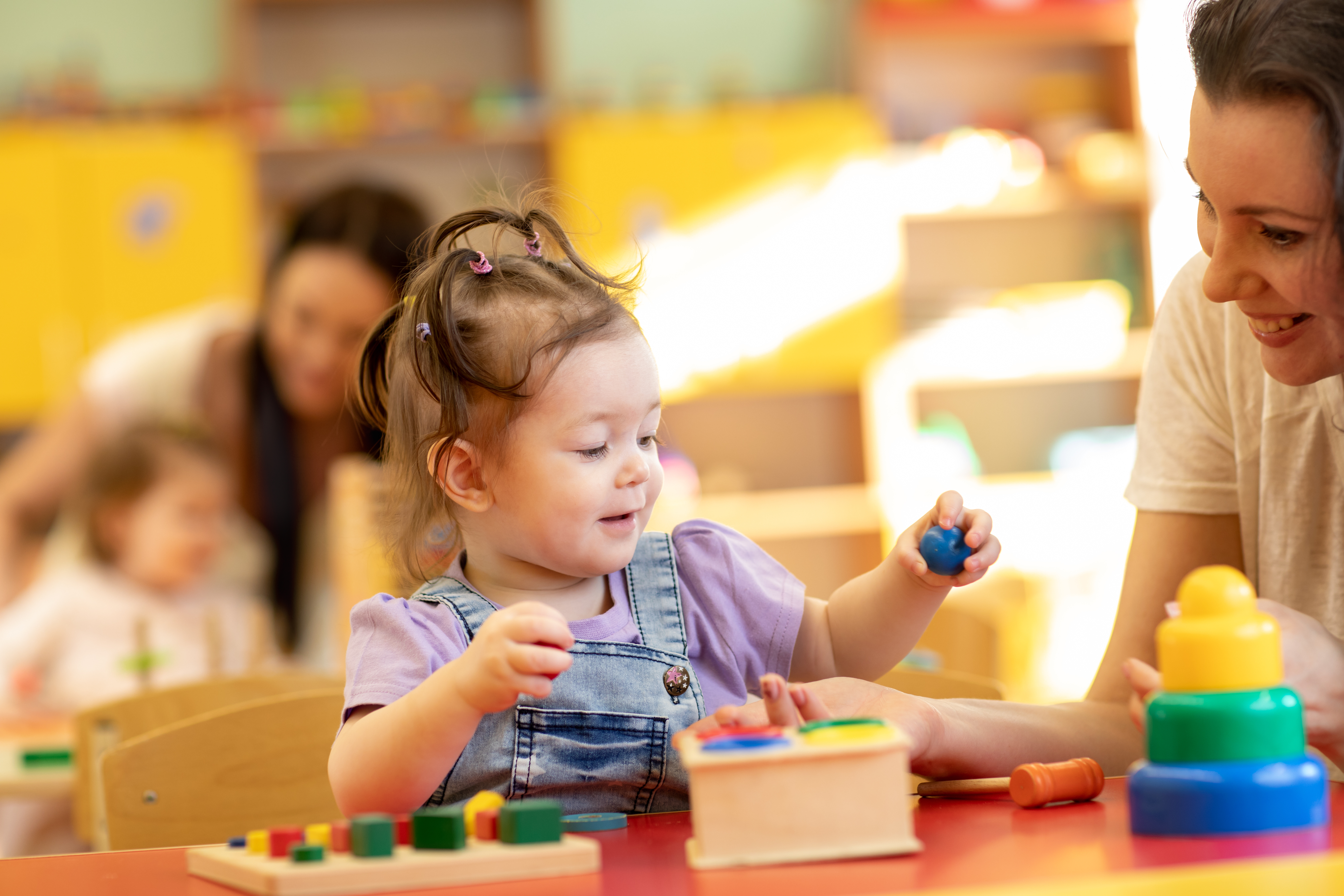 Babies with teachers playing with developmental toys in nursery