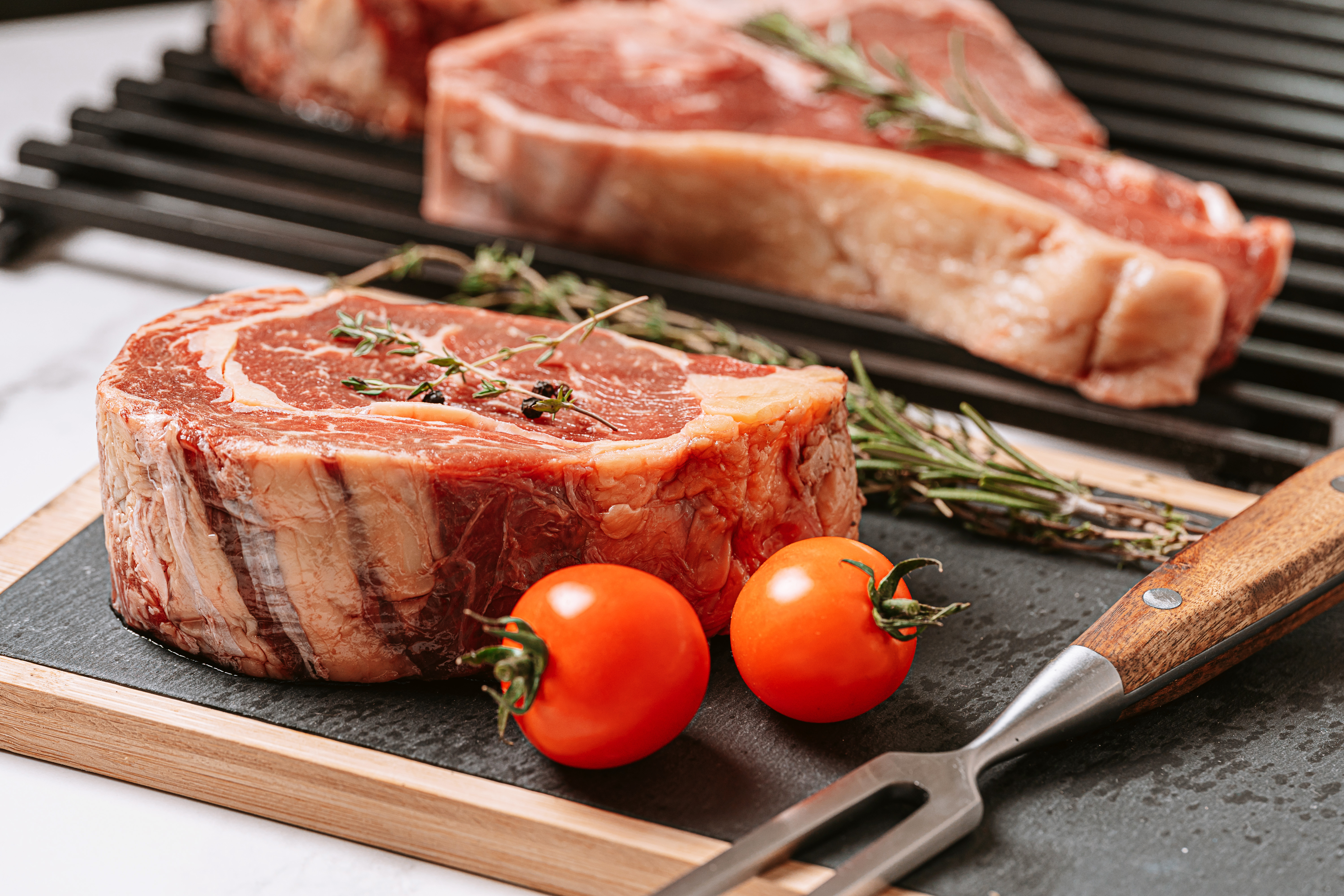 three delicious steaks ready to grill on a white marble surface