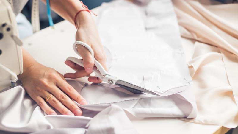 Young dressmaker cutting cloth, close up